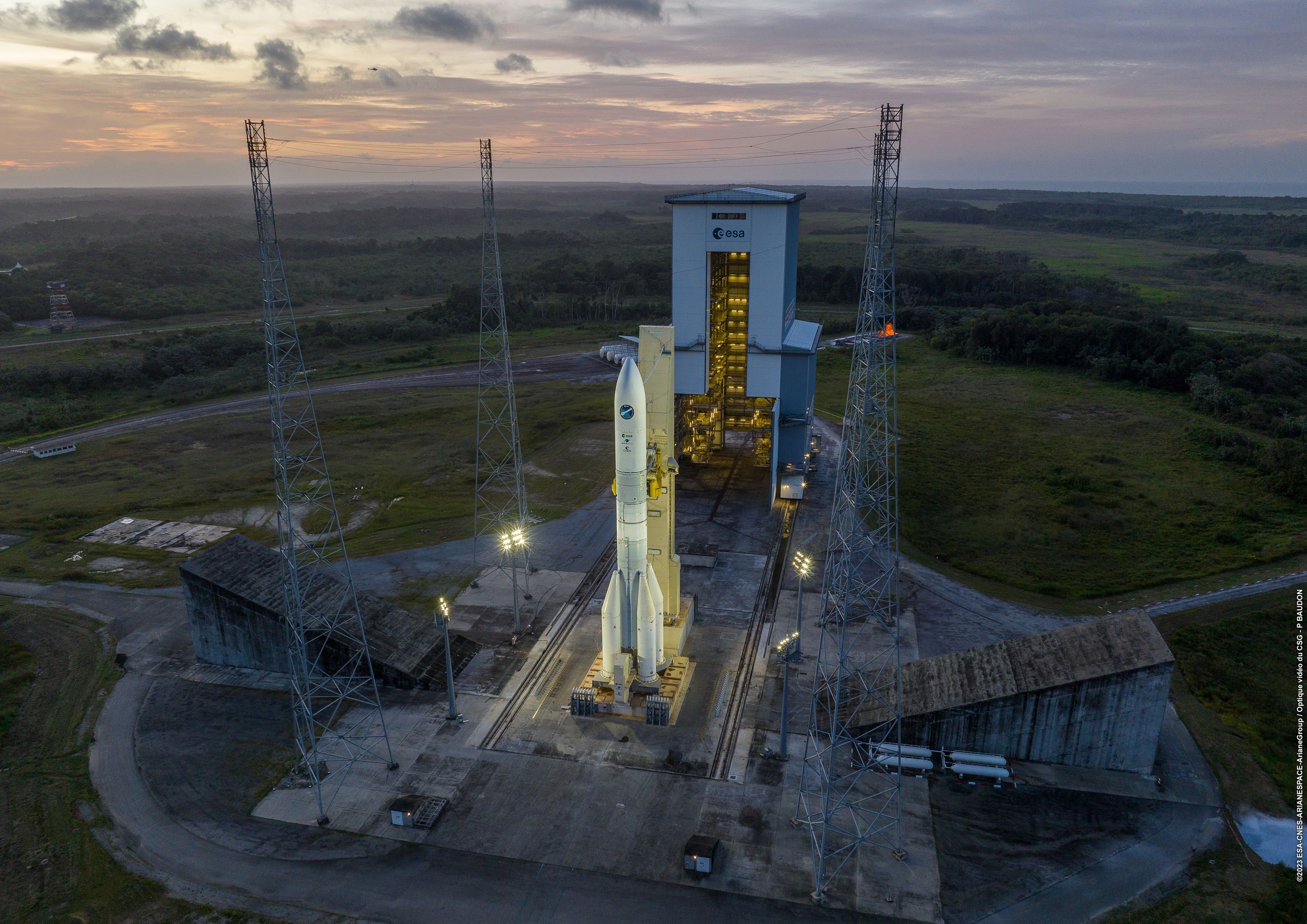 Vue au crépuscule du lanceur Ariane 6 sur son pas de tir, prêt à décoller.