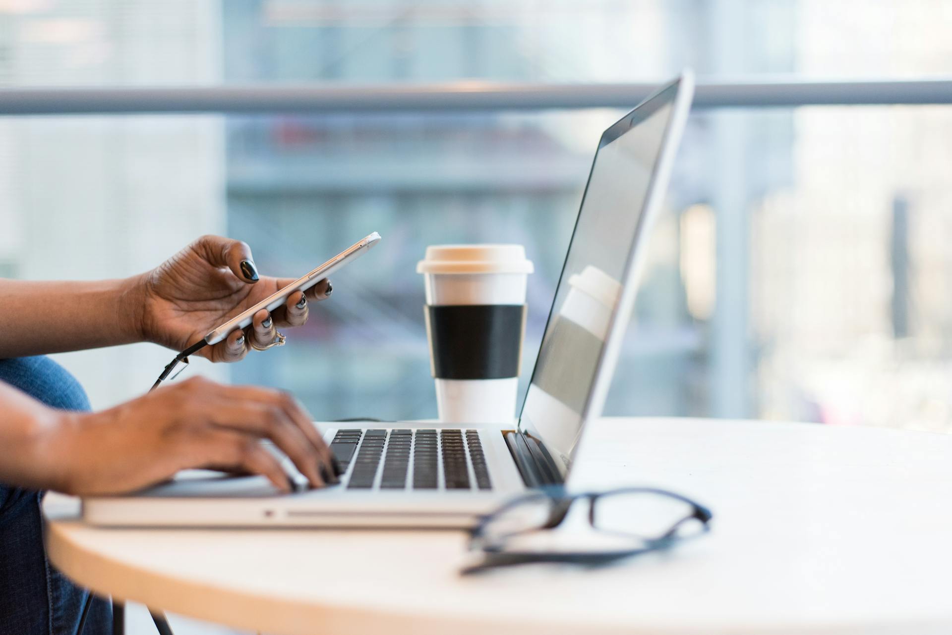 Femme tapant sur son clavier d'ordinateur avec téléphone à la main.